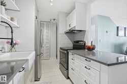 Kitchen with stainless steel appliances, white cabinetry, open shelves, under cabinet range hood, and light tile patterned floors - 