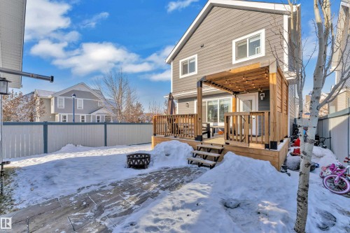 Snow covered property featuring a fenced backyard, a wooden deck, an outdoor fire pit, and a residential view - 7613 16 Ave Sw, Edmonton, AB - Outdoor With Deck Patio Veranda