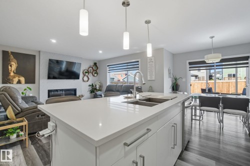 Kitchen with open floor plan, hanging light fixtures, white cabinets, a center island with sink, and dark wood-style flooring - 2039 Wonnacott Way, Edmonton, AB - Indoor Photo Showing Kitchen With Fireplace With Double Sink