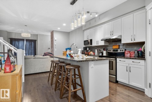 Kitchen featuring stainless steel range with electric stovetop, a breakfast bar, open floor plan, a center island with sink, and dark stone counters - 9858 72 Avenue, Edmonton, AB - Indoor Photo Showing Kitchen With Upgraded Kitchen
