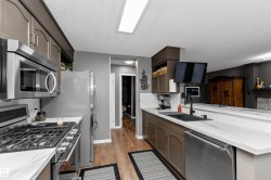 Kitchen featuring stainless steel appliances, laminate flooring, light stone counters, and a peninsula - 