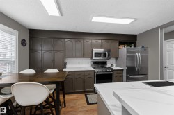 Kitchen featuring stainless steel appliances, dinette, laminate flooring, dark brown cabinetry, and light countertops - 