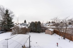 Yard covered in snow with a shed, a fenced backyard, and a residential view - 