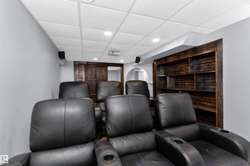 Theatre room featuring tiered seating, projector, motorized screen, and built-in shelving - 5628 188A Street, Edmonton, AB - Indoor