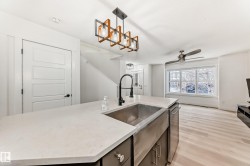 Kitchen featuring decorative light fixtures, an island with sink, light wood-style flooring, ceiling fan, and light stone counters - 