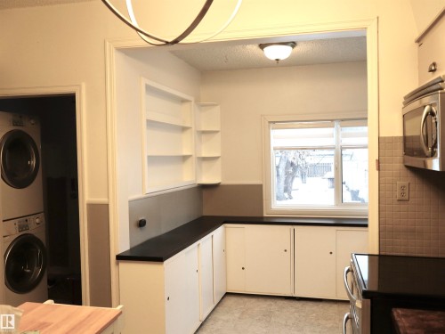 Kitchen featuring estacked washer and dryer, a textured ceiling, white cabinetry, dark countertops, and stainless steel microwave - 4511 53 Ave, Barrhead, AB - Indoor Photo Showing Laundry Room