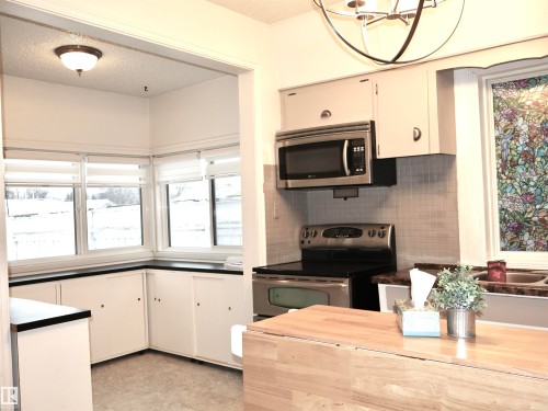 Kitchen with appliances with stainless steel finishes, a textured ceiling, white cabinetry, tasteful backsplash, and a chandelier - 4511 53 Ave, Barrhead, AB - Indoor Photo Showing Kitchen