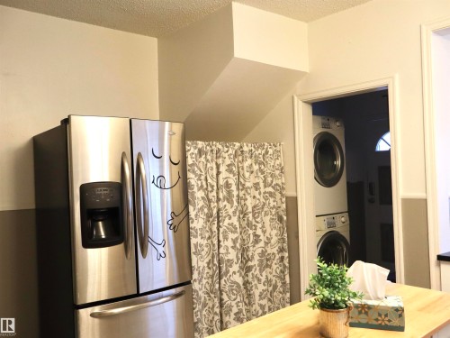 Kitchen featuring stainless steel refrigerator with ice dispenser, a textured ceiling, and stacked washing machine and dryer - 4511 53 Ave, Barrhead, AB - Indoor Photo Showing Laundry Room
