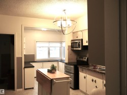 Kitchen with dark countertops, appliances with stainless steel finishes, a textured ceiling, and white cabinets - 