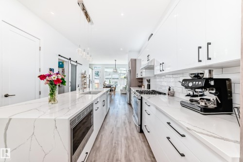 Kitchen featuring white cabinets, light stone countertops, appliances with stainless steel finishes, decorative light fixtures, and a barn door - 8321 80 Avenue, Edmonton, AB - Indoor Photo Showing Kitchen With Upgraded Kitchen