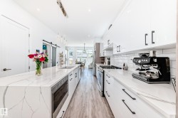 Kitchen featuring white cabinets, light stone countertops, appliances with stainless steel finishes, decorative light fixtures, and a barn door - 