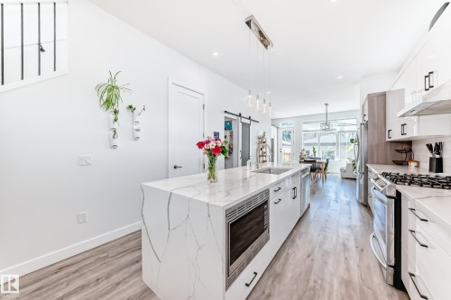 Kitchen featuring white cabinets, decorative light fixtures, light stone countertops, appliances with stainless steel finishes, and a barn door - 8321 80 Avenue, Edmonton, AB - Indoor Photo Showing Kitchen With Upgraded Kitchen