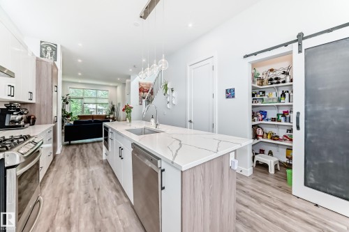 Kitchen with white cabinetry, a barn door, light stone counters, an island with sink, and appliances with stainless steel finishes - 8321 80 Avenue, Edmonton, AB - Indoor Photo Showing Kitchen With Upgraded Kitchen