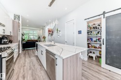 Kitchen with white cabinetry, a barn door, light stone counters, an island with sink, and appliances with stainless steel finishes - 