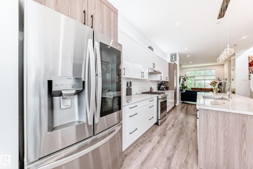 Kitchen with stainless steel appliances, modern cabinets, light stone countertops, pendant lighting, and light wood-style floors - 8321 80 Avenue, Edmonton, AB - Indoor Photo Showing Kitchen With Upgraded Kitchen