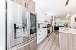 Kitchen with stainless steel appliances, modern cabinets, light stone countertops, pendant lighting, and light wood-style floors - 