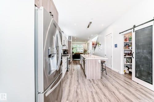 Kitchen featuring a barn door, appliances with stainless steel finishes, an island with sink, a breakfast bar, and light stone counters - 8321 80 Avenue, Edmonton, AB - Indoor