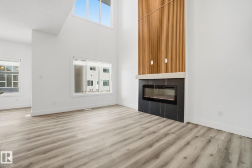 Unfurnished living room featuring a glass covered fireplace, a high ceiling, plenty of natural light, and light wood-style floors - 2532 210 Street, Edmonton, AB - Indoor Photo Showing Living Room With Fireplace