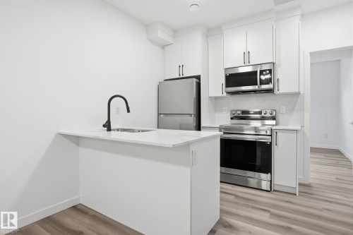 Kitchen with a peninsula, stainless steel appliances, light wood-style flooring, white cabinets, and light stone countertops - 2532 210 Street, Edmonton, AB - Indoor Photo Showing Kitchen