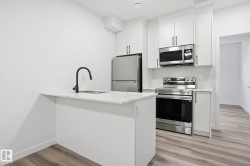 Kitchen with a peninsula, stainless steel appliances, light wood-style flooring, white cabinets, and light stone countertops - 