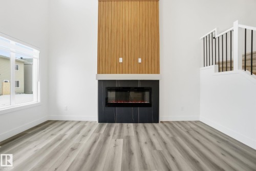 Unfurnished living room with wood finished floors, a high ceiling, stairway, and a glass covered fireplace - 2532 210 Street, Edmonton, AB - Indoor Photo Showing Living Room With Fireplace