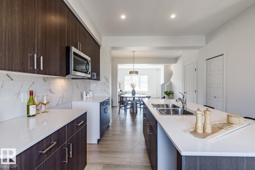 Kitchen featuring dark brown cabinetry, light stone counters, modern cabinets, stainless steel microwave, and recessed lighting - 3617 Triomphe Boulevard, Beaumont, AB - Indoor Photo Showing Kitchen With Double Sink