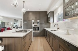 Kitchen with light stone counters, open floor plan, glass insert cabinets, appliances with stainless steel finishes, and hanging light fixtures - 