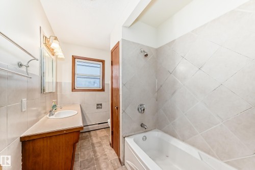 Bathroom featuring tile walls, vanity, shower / washtub combination, baseboard heating, and light tile patterned floors - 12028 87 Street, Edmonton, AB - Indoor Photo Showing Bathroom