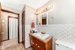 Half bath with vanity, wainscoting, tile walls, a textured ceiling, and light tile patterned floors - 