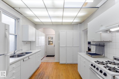Kitchen with backsplash, white appliances, white cabinets, light countertops, and healthy amount of natural light - 10921 126 Street, Edmonton, AB - Indoor Photo Showing Kitchen With Double Sink