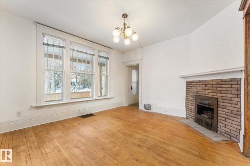 Unfurnished living room featuring light wood-style flooring, a chandelier, and a fireplace - 10921 126 Street, Edmonton, AB - Indoor With Fireplace