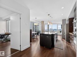 Kitchen featuring modern cabinets, decorative light fixtures, a center island with sink, dark wood-type flooring, and stainless steel appliances - 