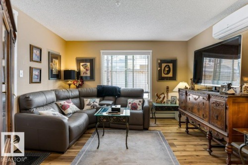 Living area with an AC wall unit, a textured ceiling, wood finished floors, and a baseboard heating unit - 107 25 Element Dr, St. Albert, AB - Indoor Photo Showing Living Room