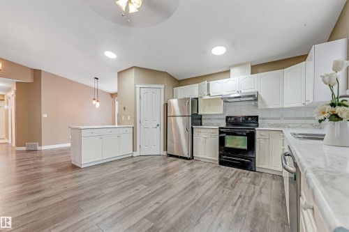 Kitchen featuring appliances with stainless steel finishes, white cabinets, decorative backsplash, pendant lighting, and under cabinet range hood - 6741 162A Avenue, Edmonton, AB - Indoor Photo Showing Kitchen With Double Sink