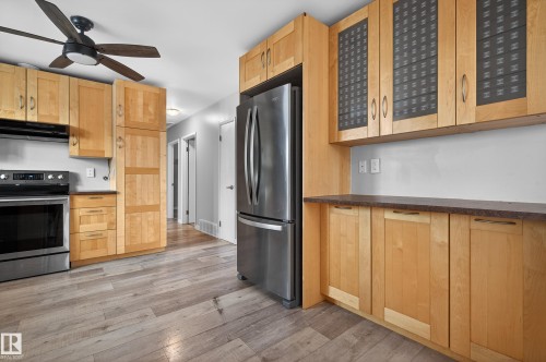 Kitchen featuring appliances with stainless steel finishes, light wood finished floors, ventilation hood, glass insert cabinets, and dark countertops - 8328 164 Street, Edmonton, AB - Indoor Photo Showing Kitchen