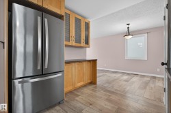 Kitchen featuring freestanding refrigerator, dark countertops, pendant lighting, glass insert cabinets, and light wood-style flooring - 