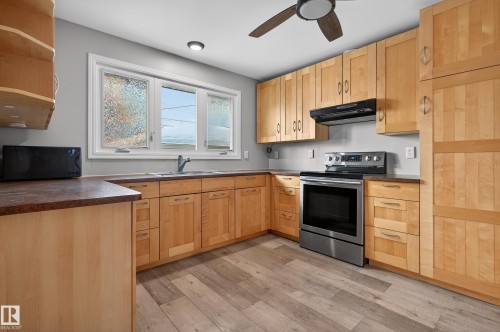 Kitchen with stainless steel range with electric stovetop, dark countertops, light brown cabinets, and under cabinet range hood - 8328 164 Street, Edmonton, AB - Indoor Photo Showing Kitchen