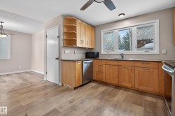 Kitchen featuring open shelves, appliances with stainless steel finishes, light wood finished floors, dark countertops, and light brown cabinets - 