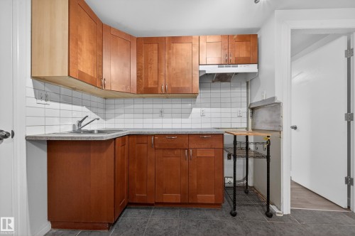 Kitchen featuring brown cabinetry, light countertops, decorative backsplash, and under cabinet range hood - 8328 164 Street, Edmonton, AB - Indoor Photo Showing Kitchen