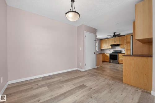 Kitchen with dark countertops, hanging light fixtures, stainless steel electric stove, light wood finished floors, and a textured ceiling - 8328 164 Street, Edmonton, AB - Indoor Photo Showing Kitchen