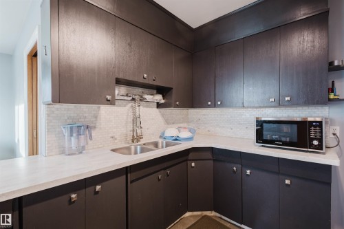 Kitchen featuring backsplash, stainless steel microwave, dark brown cabinets, and open shelves - 13315 134 Avenue, Edmonton, AB - Indoor Photo Showing Kitchen With Double Sink