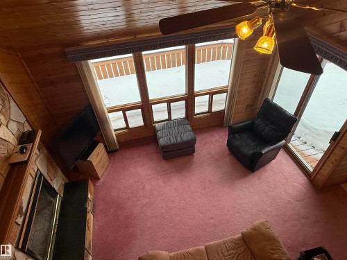 Living room featuring a stone fireplace, wood ceiling, carpet, and wooden walls - 34 Ella Mae Crescent, Athabasca Town, AB - Indoor Photo Showing Other Room