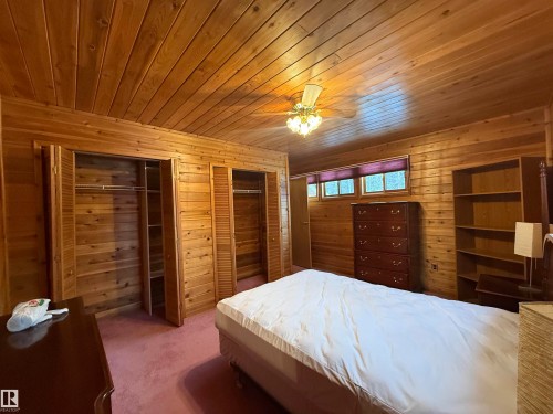 Carpeted bedroom with wooden walls, two closets, and wood ceiling - 34 Ella Mae Crescent, Athabasca Town, AB - Indoor Photo Showing Bedroom