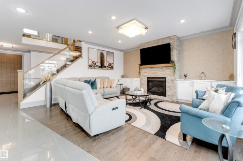 Living area with wallpapered walls, a stone fireplace, wood finished floors, crown molding, and stairway - 656 180 Street, Edmonton, AB - Indoor Photo Showing Living Room With Fireplace