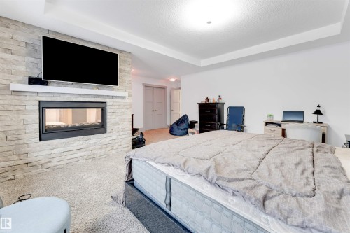 Carpeted bedroom featuring a raised ceiling, a multi sided fireplace, and a textured ceiling - 656 180 Street, Edmonton, AB - Indoor Photo Showing Bedroom With Fireplace
