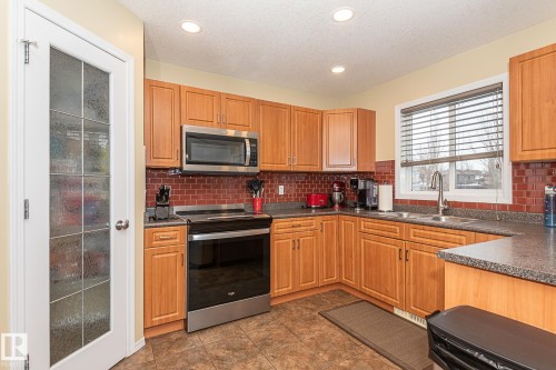 Kitchen with appliances with stainless steel finishes, dark countertops, decorative backsplash, recessed lighting, and brown cabinets - 20628 49 Avenue, Edmonton, AB - Indoor Photo Showing Kitchen With Double Sink