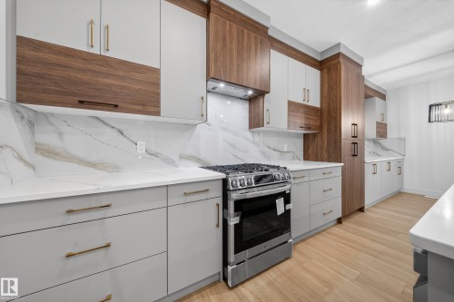 Kitchen with stainless steel gas range oven, decorative backsplash, light wood-style flooring, brown cabinetry, and white cabinetry - 6115 Crawford Drive, Edmonton, AB - Indoor Photo Showing Kitchen With Upgraded Kitchen
