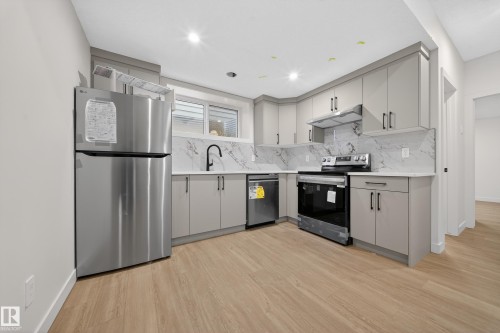 Kitchen featuring gray cabinetry, appliances with stainless steel finishes, light wood-type flooring, under cabinet range hood, and tasteful backsplash - 6115 Crawford Drive, Edmonton, AB - Indoor Photo Showing Kitchen With Stainless Steel Kitchen With Upgraded Kitchen
