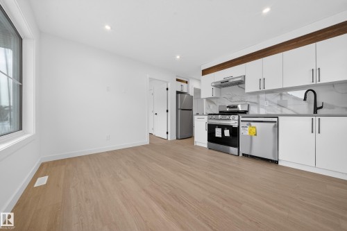 Kitchen featuring white cabinets, appliances with stainless steel finishes, light wood-type flooring, ventilation hood, and decorative backsplash - 6115 Crawford Drive, Edmonton, AB - Indoor Photo Showing Kitchen