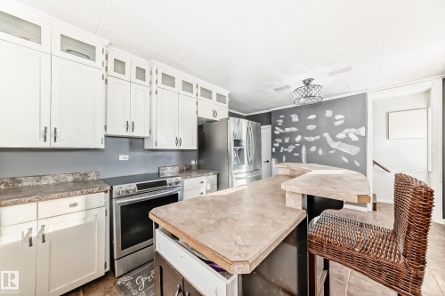Kitchen with stainless steel appliances, white cabinetry, a kitchen island, glass insert cabinets, and light countertops - 10115 104, Westlock, AB - Indoor Photo Showing Kitchen